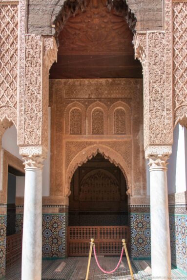 Columned carved opening leading to a tiled inner recess and wooden screen, with a rope barrier across the foreground.