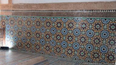 Long wall of multicolored starburst zellij above a patterned tile floor and low rectangular platform.