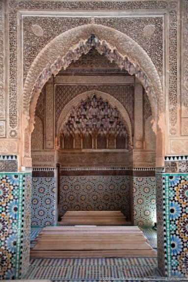 Scalloped carved arch framing a tiled funerary bay with low rectangular graves in the foreground.