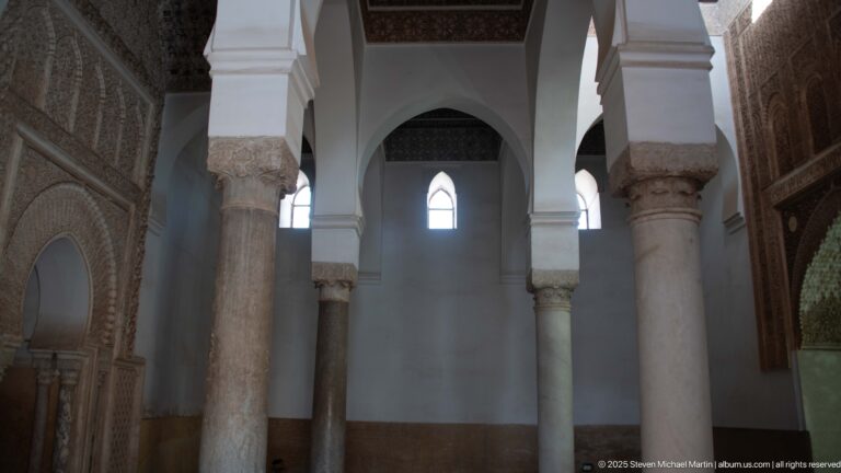 Marble columns and white arches rise between carved stucco walls inside an ornate funerary chamber.