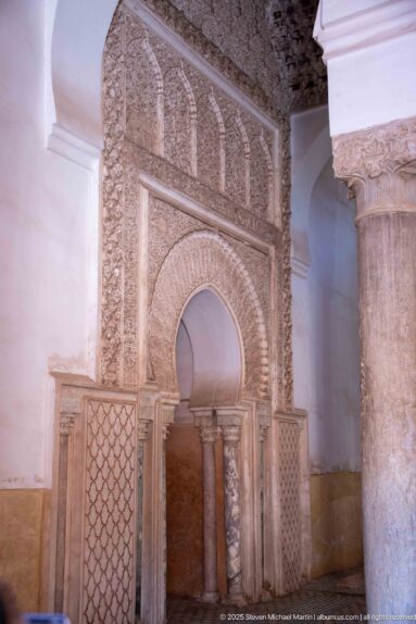 Horseshoe-arched wall niche framed by carved stucco, small columns, and geometric lattice panels.