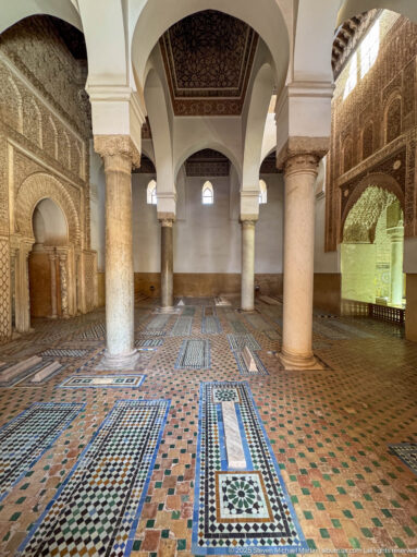 Wide view of marble columns, arches, carved walls, patterned floor, and grave markers inside the tombs.