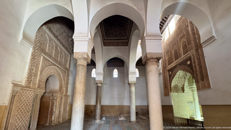 Symmetrical interior view through white arches and marble columns with carved walls on both sides.