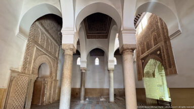 Symmetrical interior view through white arches and marble columns with carved walls on both sides.