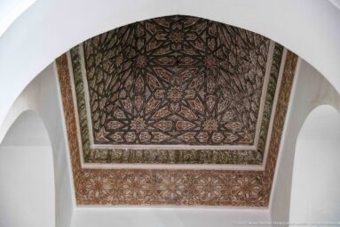 Polychrome star-patterned wooden ceiling framed by a white arch and decorated border.