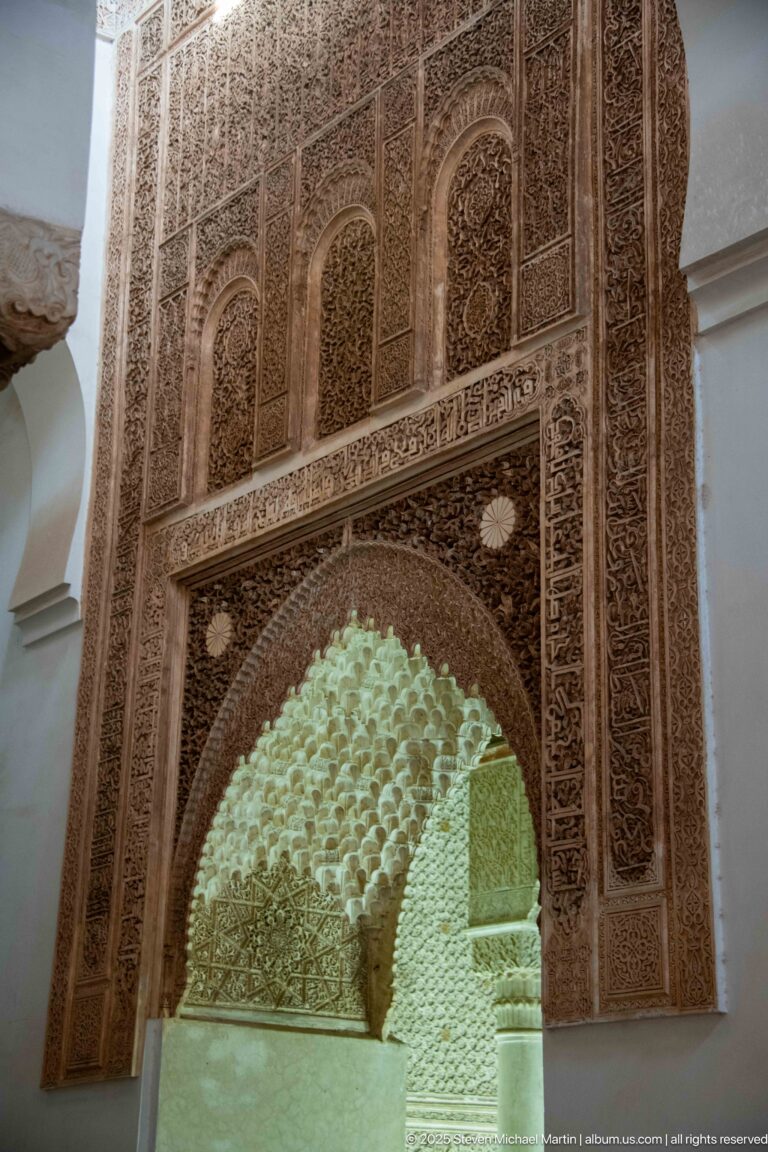 Large carved stucco arch frames a bright honeycomb-like muqarnas vault beyond.