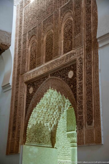 Large carved stucco arch frames a bright honeycomb-like muqarnas vault beyond.