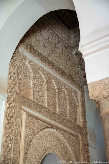 Upper carved stucco wall with blind arches and floral relief above a horseshoe arch.