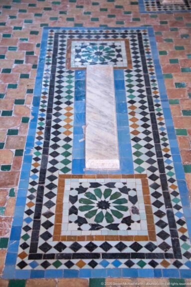 Pale rectangular grave marker centered in a multicolored geometric zellij mosaic panel.