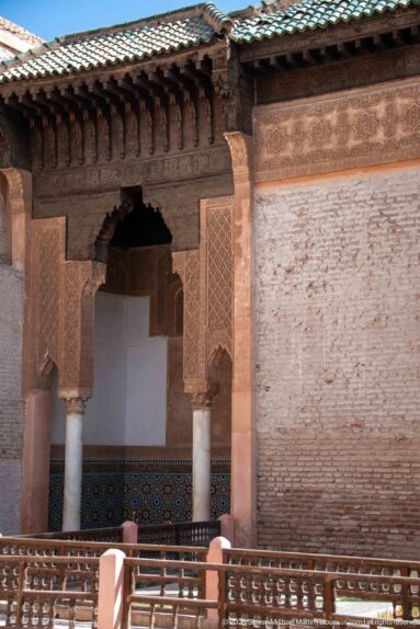 Courtyard pavilion with green tile roof, carved wooden eaves, columns, and a shaded arched opening.