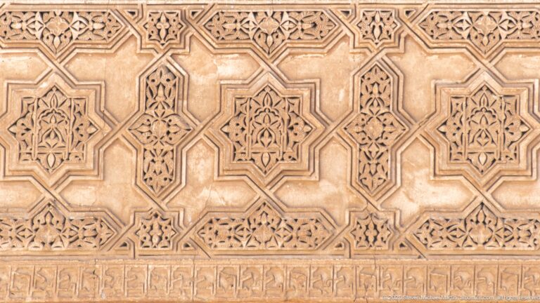 Close-up of carved wooden panel with interlocking geometric star forms and small floral motifs.