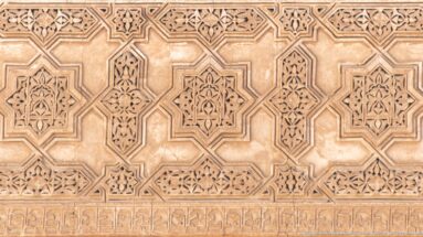Close-up of carved wooden panel with interlocking geometric star forms and small floral motifs.