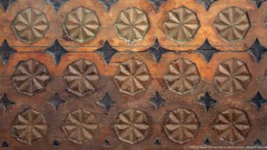 Warm wooden panel patterned with rows of raised rosettes and small dark diamond motifs.