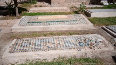 Two raised tiled graves, including a foreground geometric mosaic with a visibly damaged patch of loose tiles.
