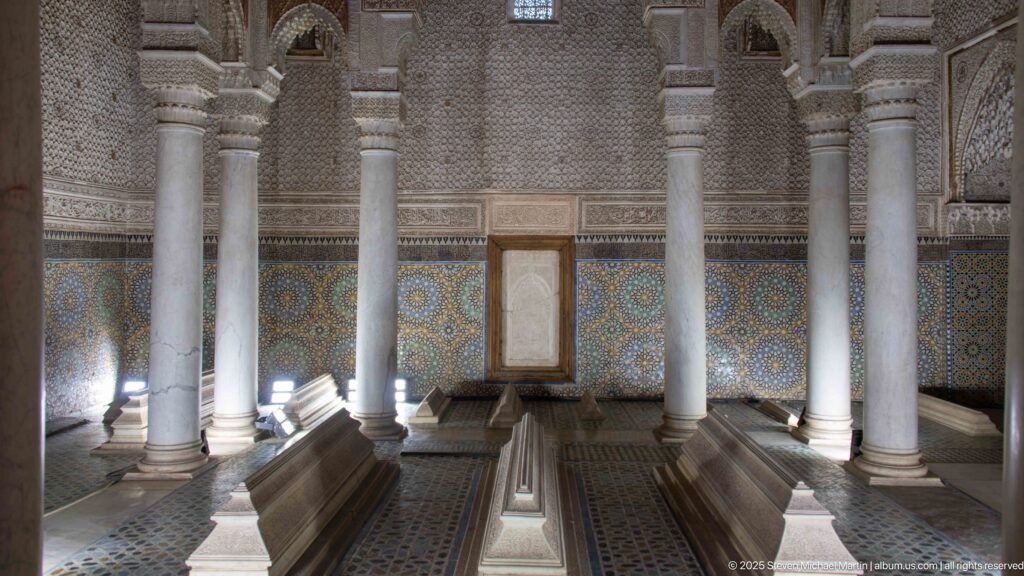 Raised marble tombs stand among columns inside a chamber lined with zellij and carved stucco.