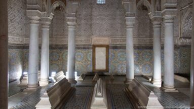 Raised marble tombs stand among columns inside a chamber lined with zellij and carved stucco.
