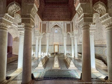 Wide symmetrical view of tombs, marble columns, carved arches, zellij walls, and dark wooden ceiling.