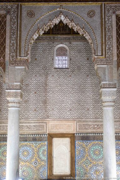 Scalloped carved stucco arch rises above blue-green zellij and a central rectangular wall panel.