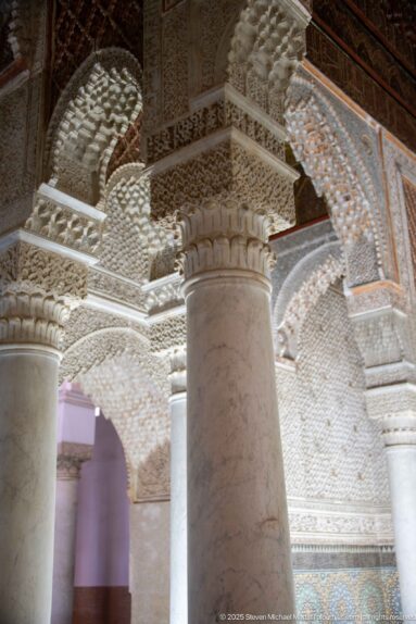 Close oblique view of a marble column meeting a deeply carved stucco capital and arches.