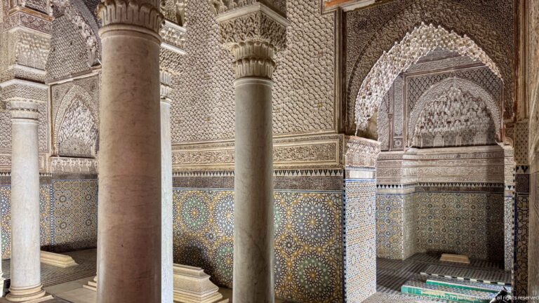 Pointed muqarnas alcove above geometric zellij, partly framed by marble columns.