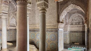 Pointed muqarnas alcove above geometric zellij, partly framed by marble columns.