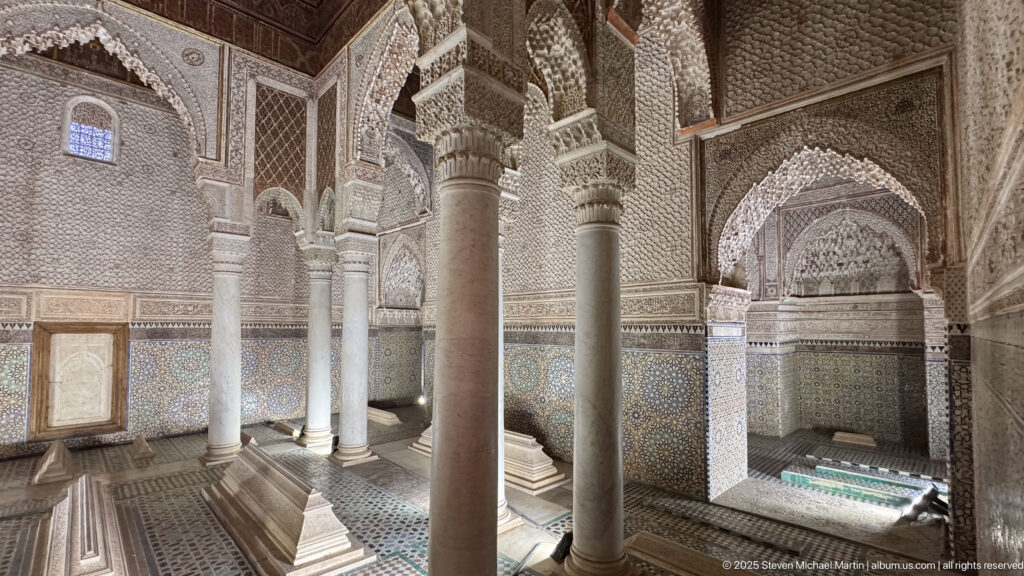 Slender columns, carved arches, tiled walls, and low tomb markers inside an ornate mausoleum chamber.