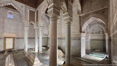 Slender columns, carved arches, tiled walls, and low tomb markers inside an ornate mausoleum chamber.