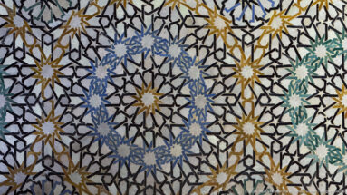 Close-up of polychrome zellij mosaic with interlaced black lines, starbursts, and blue, green, ochre, and white pieces.
