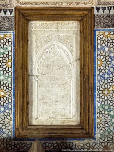 Framed pale carved panel with Arabic script bordered by multicolored geometric zellij.
