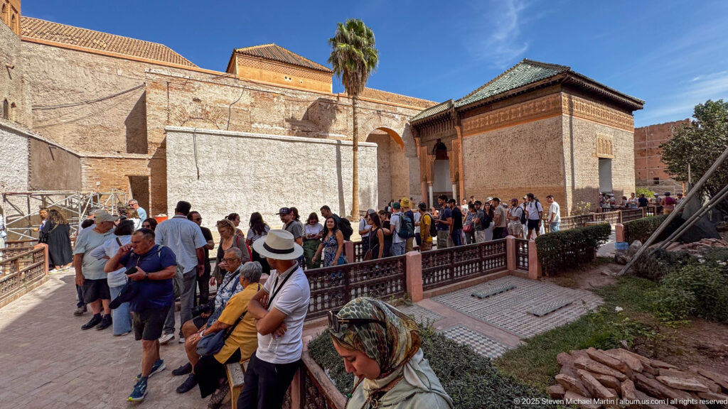 Crowd of visitors waiting along a railing beside ochre walls and tile-roofed buildings at the Saadian Tombs.