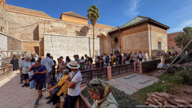 Crowd of visitors waiting along a railing beside ochre walls and tile-roofed buildings at the Saadian Tombs.