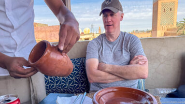 Server holding a terracotta pitcher beside a seated diner at an outdoor terrace table in Marrakech.