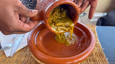 Thick yellow-green stew pouring from a small terracotta pot into a wide clay dish.