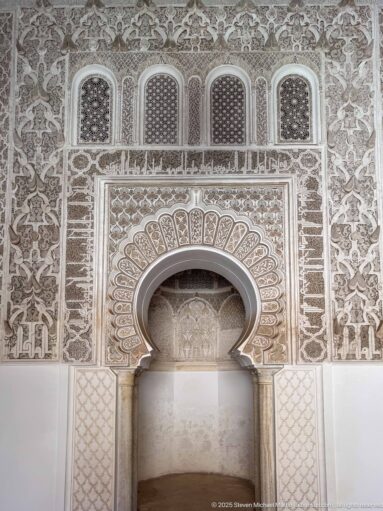 Symmetrical carved stucco wall with central horseshoe niche and small arched lattice openings above.