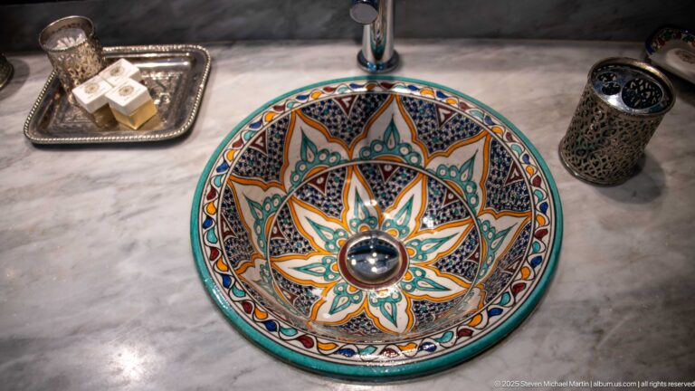 Hand-painted ceramic vessel sink with turquoise, orange, black, and white floral-geometric decoration on a marble counter.