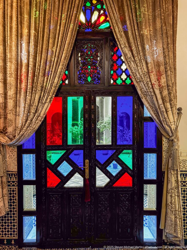 Closed dark-wood double doors filled with multicolored glass panels and framed by heavy gold-toned curtains.