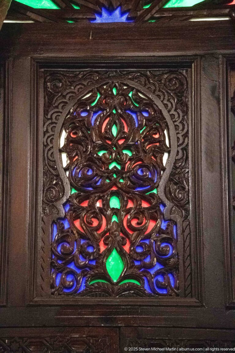 Close-up of pierced dark wood carving inset with red, blue, green, and clear glass, including a green diamond.