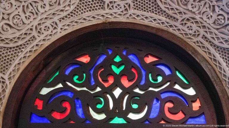 Close-up of red, blue, green, and white glass fanlight beneath dense white carved plaster ornament.