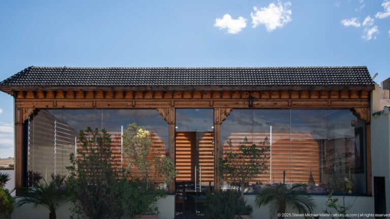 Glass-walled timber pavilion with tiled roof and potted plants on a terrace at Riad Fes Maya.
