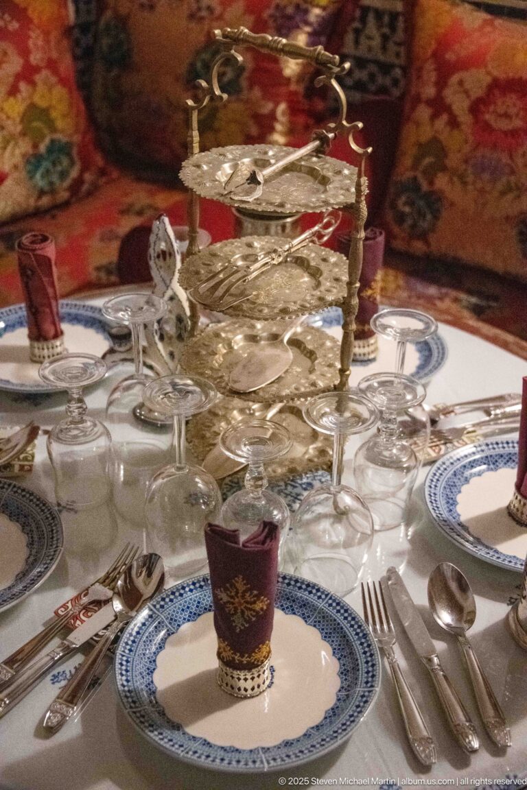 Formal dining table with blue-and-white plates, red glasses, clear stemware, polished cutlery, and an ornate tiered metal stand.