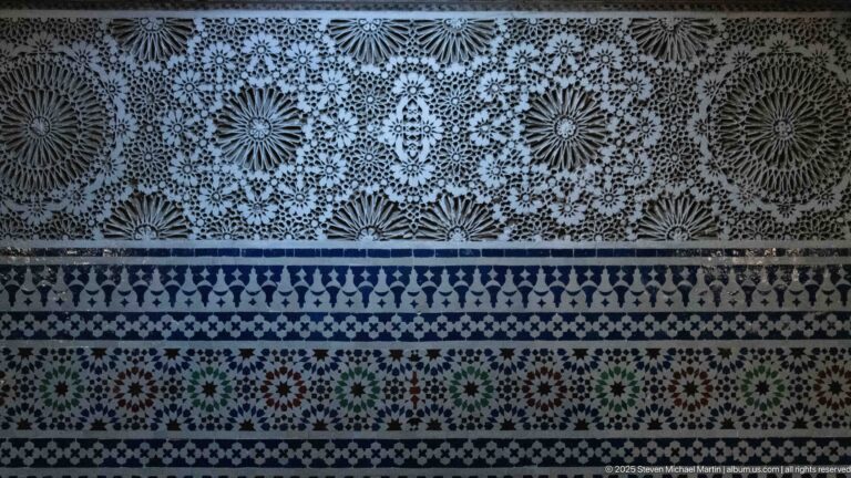 Close wall detail of pale floral carved plaster above blue, white, green, and red geometric zellij bands.