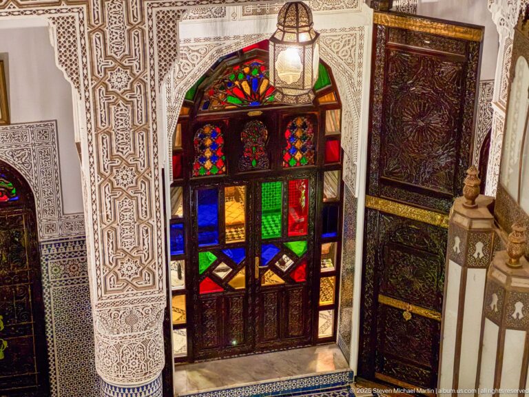 Oblique upper-level view of a multicolored glazed doorway with carved wood, patterned plaster, and adjacent decorative paneling.