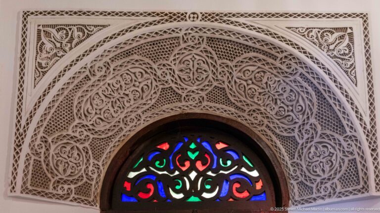 Close-up of a multicolored glass fanlight beneath an intricately carved plaster arch and dark wooden frame.