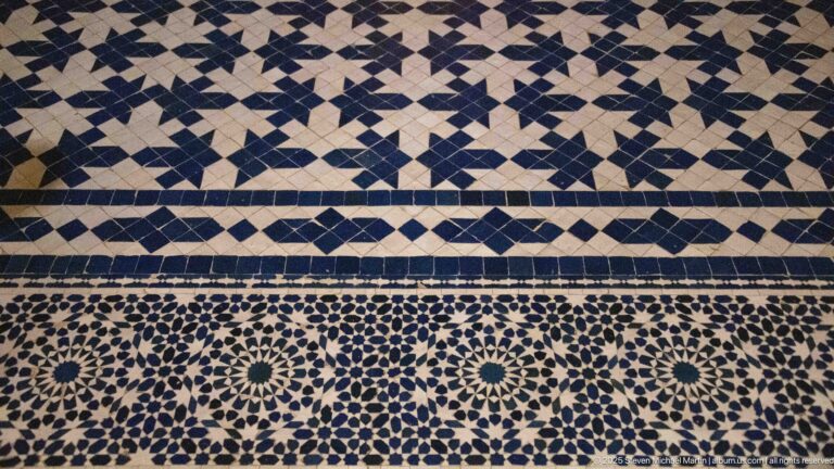 Close blue-and-white zellij wall panel with star rosettes, diamonds, and narrow geometric border bands.