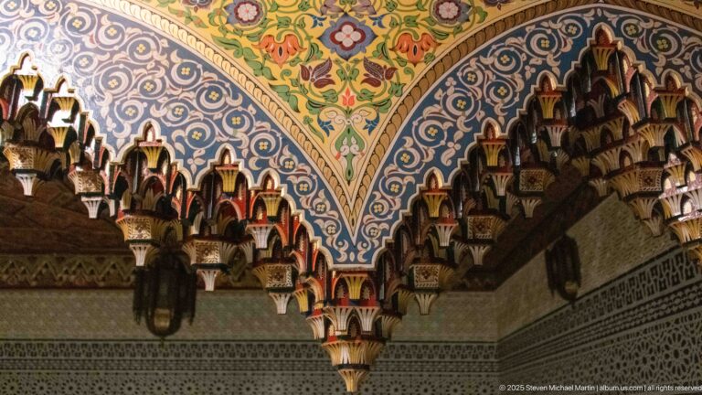Polychrome stalactite-like carved wooden corbels beneath a painted floral and geometric ceiling.