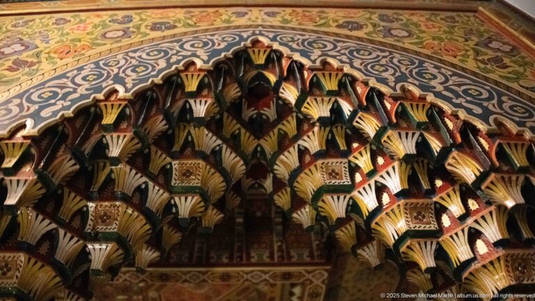 Close detail of layered multicolored wooden corbels beneath a decorated ceiling border.