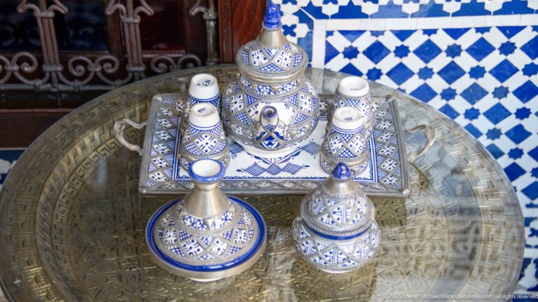 Blue-and-white ceramic tea service with small cups and metal vessels arranged on a large engraved brass tray.