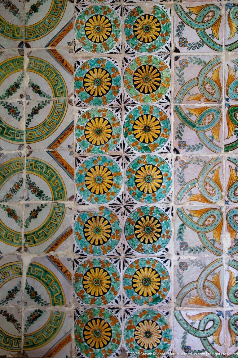 Close view of palace tiles arranged in bands of yellow rosettes, green interlace, and oval geometric medallions.