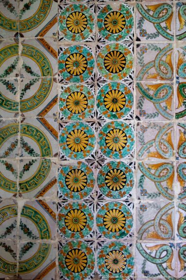 Close view of palace tiles arranged in bands of yellow rosettes, green interlace, and oval geometric medallions.