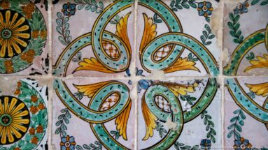 Close-up of a four-lobed turquoise, green, and ochre tile motif with visible cracks, chips, and grout lines.